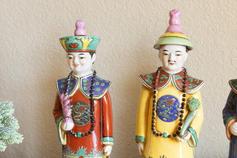 May include: Two porcelain figurines of people wearing traditional Chinese clothing. The figurines are painted in bright colors, including red, yellow, blue, and green. They are holding objects in their hands, and their faces are painted with expressions of serenity.