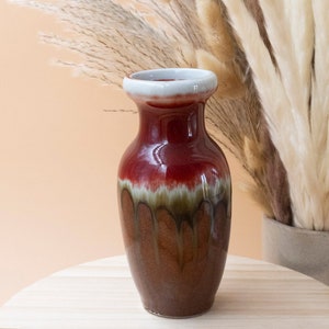 May include: A red and brown ceramic vase with a white rim. The vase has a mottled glaze and a rounded shape.