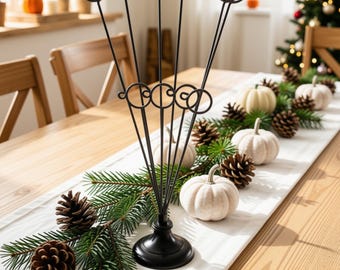 May include: A black metal card holder stand featuring four tall, thin stems with circular loops at the top and middle, supported by a round, weighted base. The stand is constructed from slender wire and has a matte black finish throughout its structure.