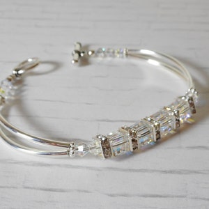 May include: A silver bangle bracelet with a row of clear crystal beads and a silver toggle clasp.