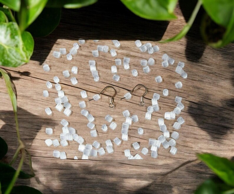 May include: A close-up of a wooden surface with a scattering of small, white, plastic beads. Two silver earring hooks are placed in the centre of the image.