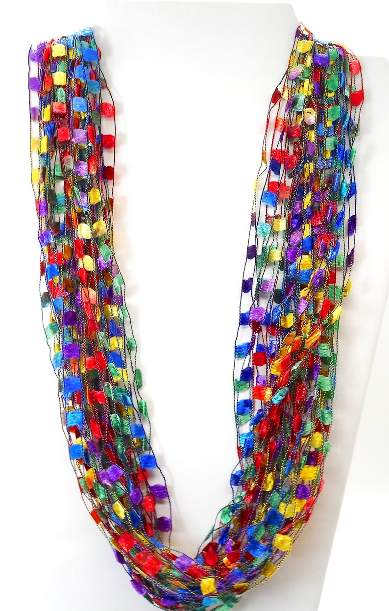 May include: A multi-strand necklace made of thin, woven strands of yarn with small, square-shaped beads in shades of red, orange, yellow, green, blue, purple, and black.