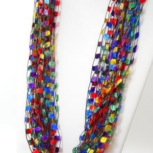 May include: A multi-strand necklace made of thin black thread with small squares of various colours, including red, blue, green, yellow, and purple.