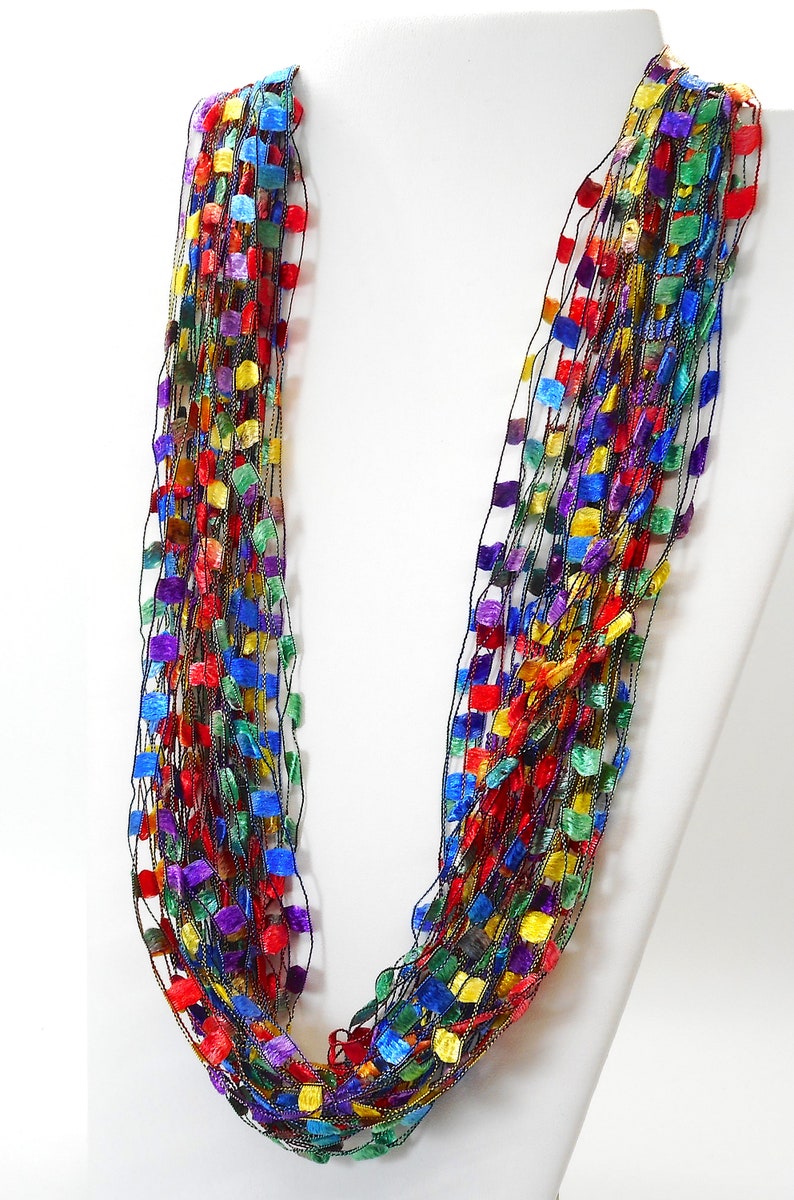 May include: A multi-strand necklace made of thin black thread with small squares of various colours, including red, blue, green, yellow, and purple.
