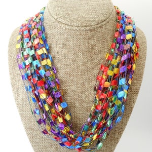 May include: A multi-coloured crocheted necklace featuring a range of colours including red, blue, green, yellow, and purple. The necklace is crafted from thin strands of yarn that are crocheted together to create a series of small squares.