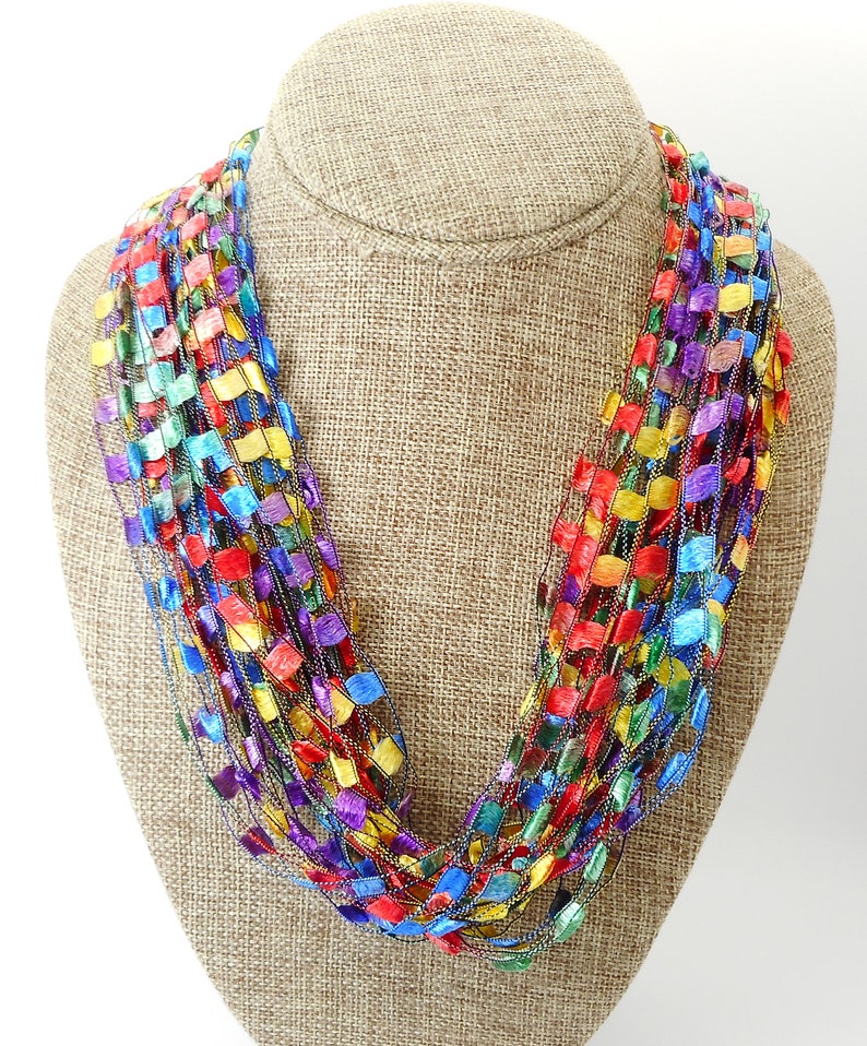 May include: A multi-coloured crocheted necklace featuring a range of colours including red, blue, green, yellow, and purple. The necklace is crafted from thin strands of yarn that are crocheted together to create a series of small squares.
