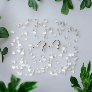 May include: Two gold earring hooks with clear silicone earring backs scattered around them on a white surface.
