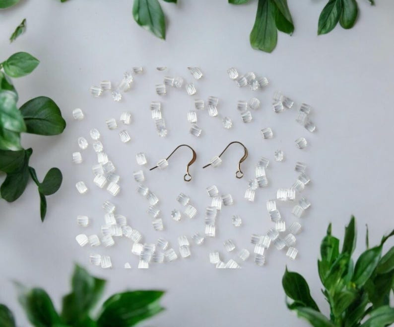 May include: Two gold earring hooks with clear silicone earring backs scattered around them on a white surface.