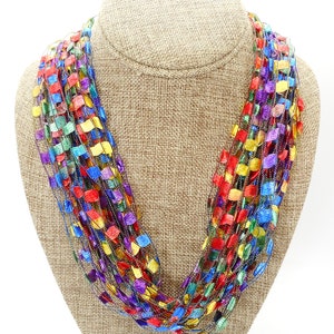 May include: A multi-coloured crocheted necklace with a metallic sheen. The necklace is made of a variety of colours, including red, orange, yellow, green, blue, and purple.