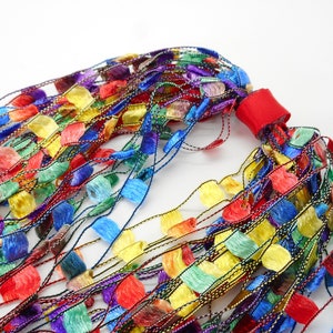 May include: A colourful, multi-strand necklace made of thin, woven strands with small, fringed, fabric pieces in various colours, including red, yellow, blue, green, and purple.