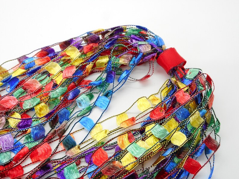 May include: A colourful, multi-strand necklace made of thin, woven strands with small, fringed, fabric pieces in various colours, including red, yellow, blue, green, and purple.