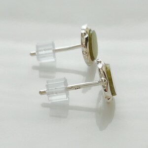 May include: A pair of silver earrings with green gemstone accents. The earrings have a simple design and are perfect for everyday wear.