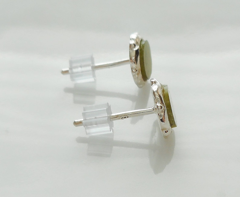 May include: A pair of silver earrings with green gemstone accents. The earrings have a simple design and are perfect for everyday wear.