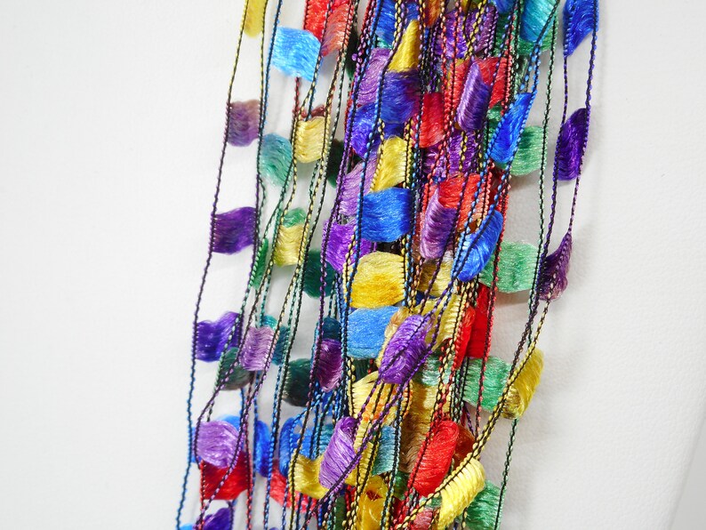 May include: A multi-coloured yarn with a fringe texture. The yarn is made up of multiple strands of different colours, including red, blue, green, yellow, and purple.