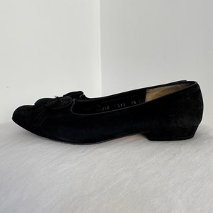 K&ouml;nnte beinhalten: Schwarze Ballerinas aus Wildleder mit einem kleinen Quasten-Detail an der Spitze. Die Ballerinas haben einen niedrigen Absatz und sind mit der Gr&ouml;&szlig;e 311 7 1/2 gekennzeichnet.