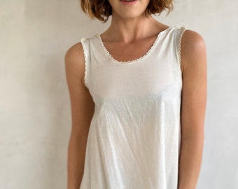 May include: A white sleeveless top with a scalloped lace trim around the neckline and hem. The top is made of a lightweight fabric and has a relaxed fit.