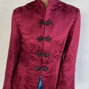 May include: A burgundy silk jacket with a mandarin collar and decorative floral pattern. The jacket has a front closure with multiple black buttons.