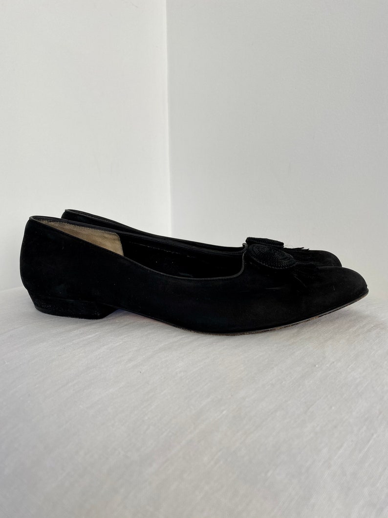 K&ouml;nnte beinhalten: Schwarze Ballerinas aus Wildleder mit einem kleinen schwarzen Quasten-Detail an der Spitze.