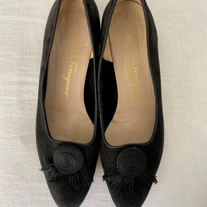 K&ouml;nnte beinhalten: Ein Paar schwarze Wildlederschuhe mit einem schwarzen Quasten und einem schwarzen Seildetail an der Spitze. Die Schuhe sind innen mit "Salvatore Ferragamo" beschriftet.