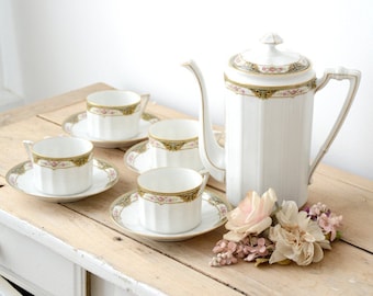 May include: A white porcelain tea set with a gold and pink floral design. The set includes a teapot, four cups, and four saucers.