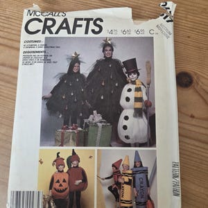 May include: A McCall's Crafts sewing pattern envelope featuring illustrations of costumes including a Christmas tree, a snowman, pumpkins, and crayons. The white paper envelope displays text and images of people wearing these various costumes.
