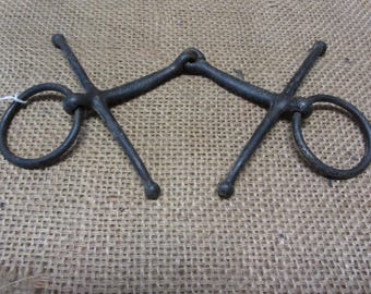 May include: A black metal horse bit with two rings and four arms. The bit is designed to fit in a horse's mouth and is used to control the horse.