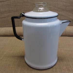 May include: White enamel coffee pot with a black handle and trim. The pot has a clear glass top and a spout for pouring. A classic kitchenware item.