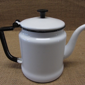 May include: White enamelware coffee pot with a black handle, lid knob, and rim. The spout is curved and the pot has a rounded body. A classic kitchenware item.