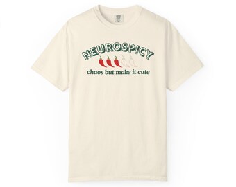 Può includere: T-shirt color crema con la scritta "NEUROSPICY" in verde, arcuata sopra la frase "chaos but make it cute". Sotto la parola "NEUROSPICY" ci sono tre peperoncini rossi e un peperoncino bianco.