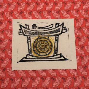 May include: A black and white linocut print of a Japanese temple gate with a golden circle in the center. The print is on a white background and is framed by a white border.