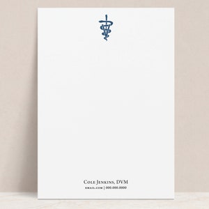 May include: A white notepad with a blue medical symbol at the top and the text "COLE JENKINS, DVM" and "EMAIL.COM | 000.000.0000" at the bottom.