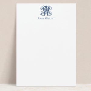 May include: White stationery with a navy blue monogram and the name "Anne Wright" printed below. The monogram is an ornate design with the letters "AW" intertwined. The paper is blank and ready for writing.