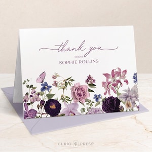 May include: A folded white card with a floral design and the words "thank you" and "from SOPHIE ROLLINS" in purple script. The floral border features purple, pink, and blue flowers, and a butterfly. The card is inside a lavender envelope.