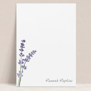May include: A white notepad with a watercolor illustration of lavender flowers in the upper left corner. The name "Hannah Hopkins" is written in cursive at the bottom of the page.
