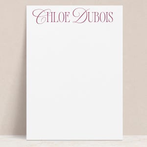 May include: White notepad with the name "CHLOE DUBOIS" printed in burgundy cursive script at the top.