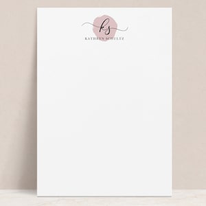 May include: A white notepad with a pink circle and the initials "KS" in black script. The text "KATHRYN SCHULTZ" is printed below the circle.