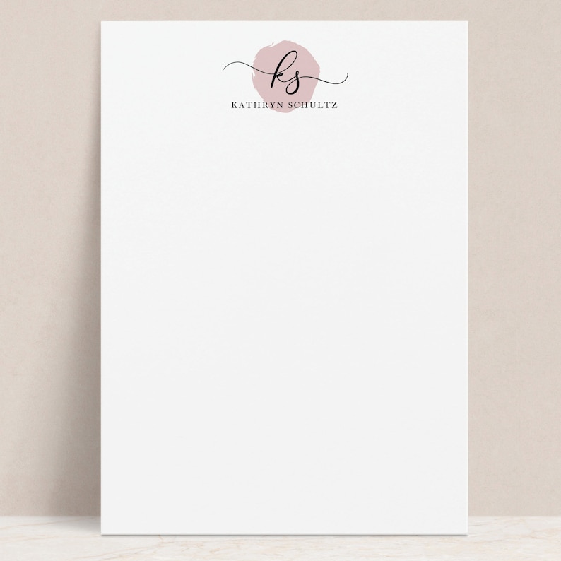 May include: A white notepad with a pink circle and the initials "KS" in black script. The text "KATHRYN SCHULTZ" is printed below the circle.