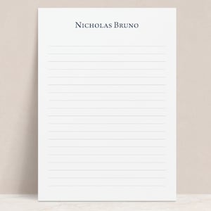 May include: A white lined notepad with the name "Nicholas Bruno" printed in dark blue at the top.