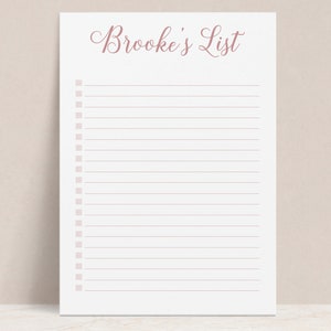 May include: A white notepad with the text "Brooke's List" in a cursive font at the top. The notepad has horizontal lines and check boxes down the left side, all in a soft rose color.