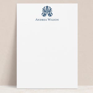 May include: White stationery with a navy blue monogram and the name "Andrea Wilson" printed below. The monogram is an ornate design, adding a touch of elegance to the paper. The design is centered at the top of the page.