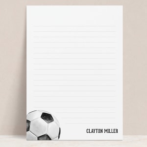 May include: A white and black soccer ball with a black and white striped design. The ball is on a white sheet of paper with lines. The text "CLAYTON MILLER" is at the bottom of the page.