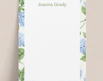 Puede incluir: Papelería con diseño floral. El borde presenta flores de hortensia azules y hojas verdes sobre un fondo crema. El texto "Joanna Grady" está impreso en verde en la parte superior.