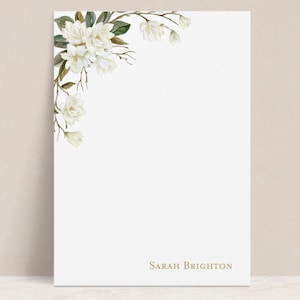 May include: White stationery with a watercolor floral design in the upper left corner. The design features white flowers, green leaves, and brown branches. The name "Sarah Brighton" is printed in gold at the bottom.