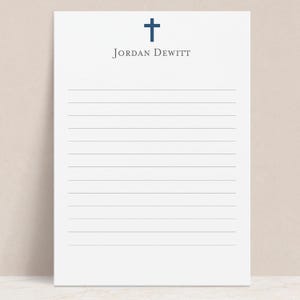May include: White notepad with lined paper and a blue cross at the top. The name "JORDAN DEWITT" is printed below the cross.