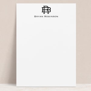 May include: White notepad with a black monogram of the letters "BR" and the text "BRYAN ROBINSON" printed at the top.
