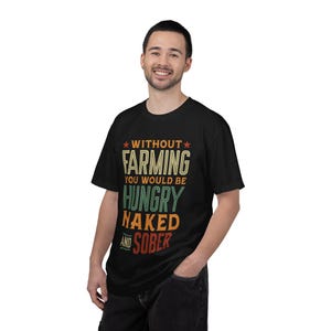 Puede incluir: Camiseta negra con el texto "WITHOUT FARMING YOU WOULD BE HUNGRY NAKED AND SOBER" en un estilo vintage. El texto es de varios colores, incluyendo verde, naranja y blanco. La camiseta la lleva una persona.