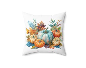 Puede incluir: Cojín cuadrado blanco con un diseño de acuarela de calabazas, hojas y bayas. Las calabazas son de varios tamaños y colores, incluyendo naranja, azul claro y crema. El follaje otoñal rodea las calabazas, creando un tema estacional.