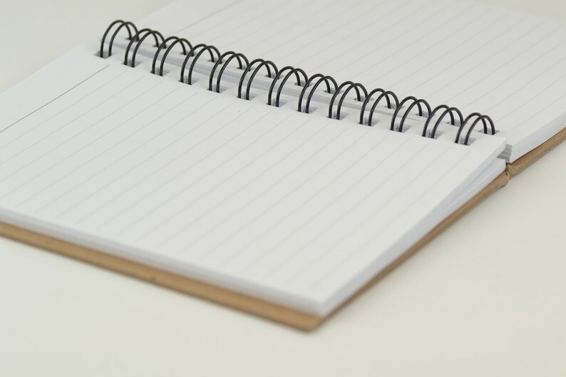May include: A blank, lined notebook with a black wire-o binding. The notebook has a brown cardboard cover.