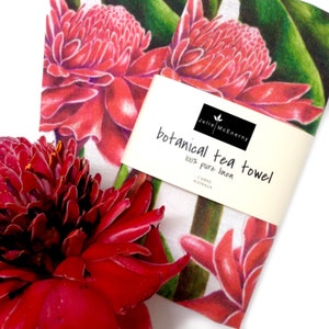 May include: Two red and white botanical tea towels with a green floral design. The towels are made of 100% pure linen and are from Cairns, Australia. The text on the tag reads "Julie McEnerny botanical tea towel 100% pure linen Cairns Australia."
