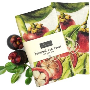 May include: Two linen tea towels with a botanical illustration of mangosteens. The towels are white with a green and brown border. The text on the label reads "botanical tea towel 100% pure linen Cabin Australia".